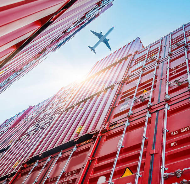 Plane flying over red shipping containers